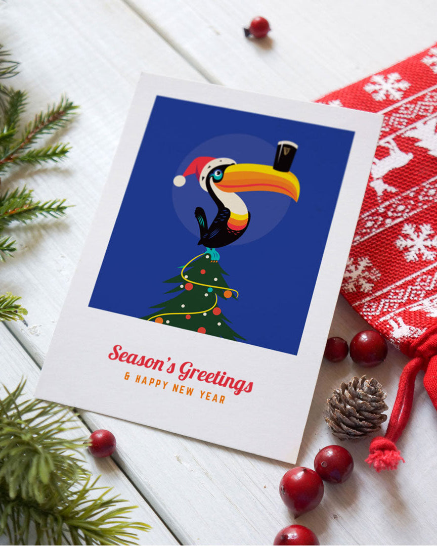 Christmas card with a toucan and Christmas tree design, surrounded by festive decorations on a white surface.
