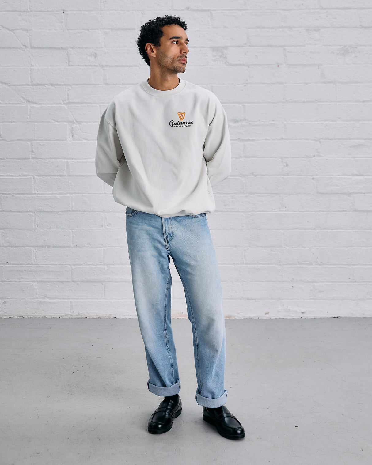Man wearing a light gray 'Guinness' sweatshirt against a white brick wall.