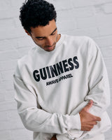 Man wearing a white sweatshirt with 'Guinness Awave Apparel' text against a gray brick wall.