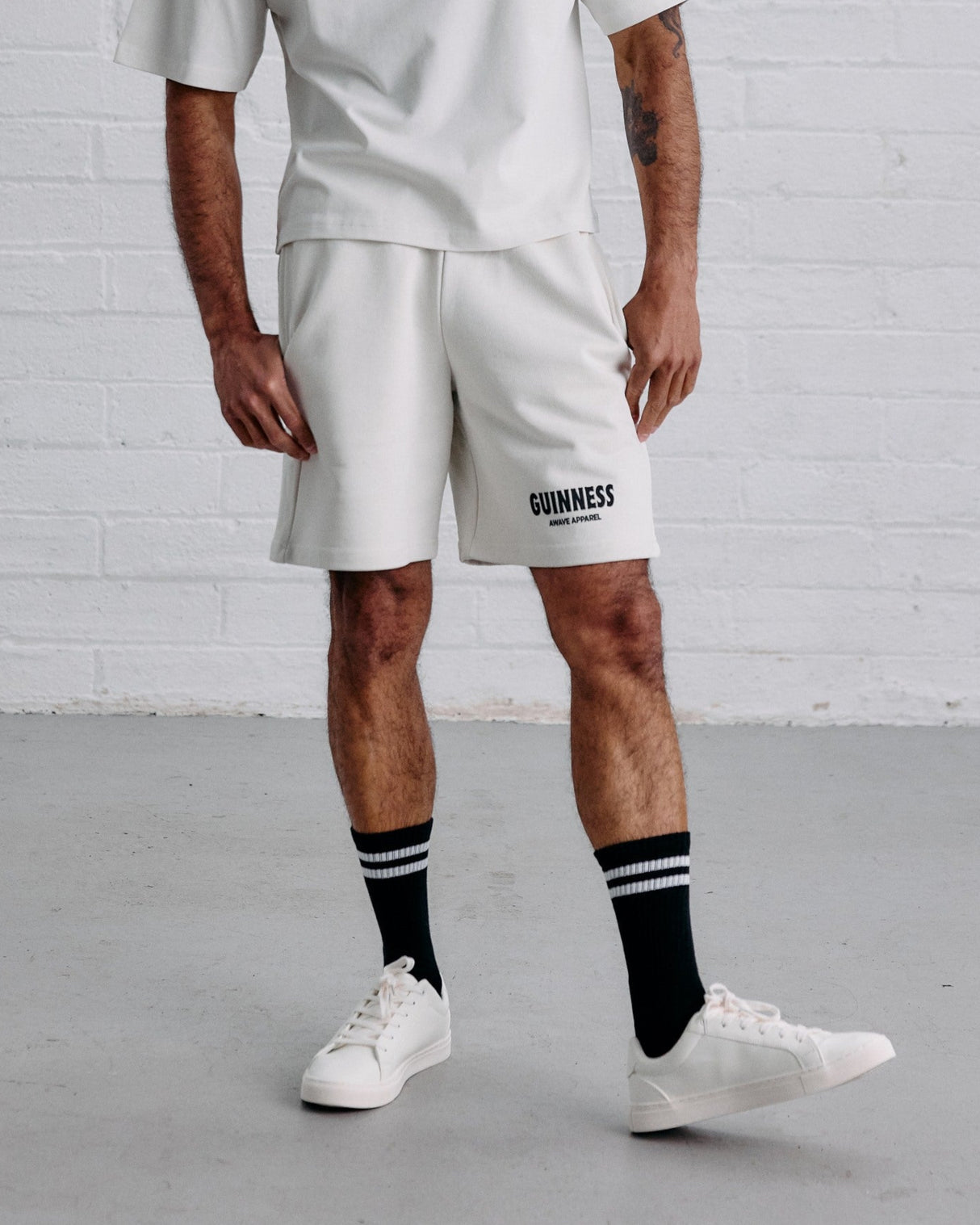 Man wearing a white t-shirt and shorts with 'Guinness' branding against a white brick wall.