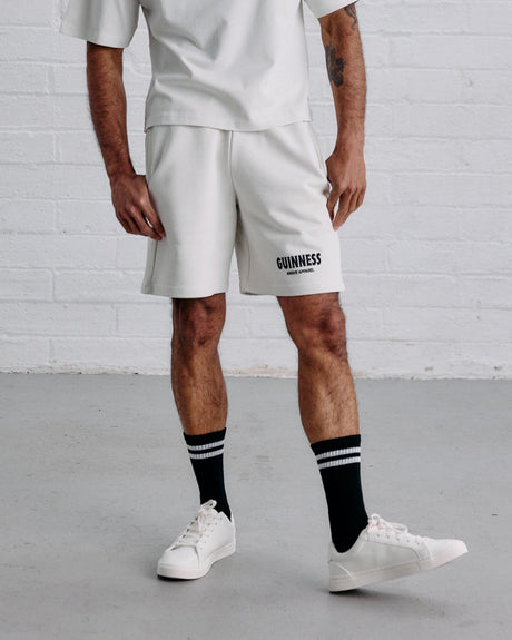 Man wearing a white t-shirt and shorts with 'Guinness' branding against a white brick wall.