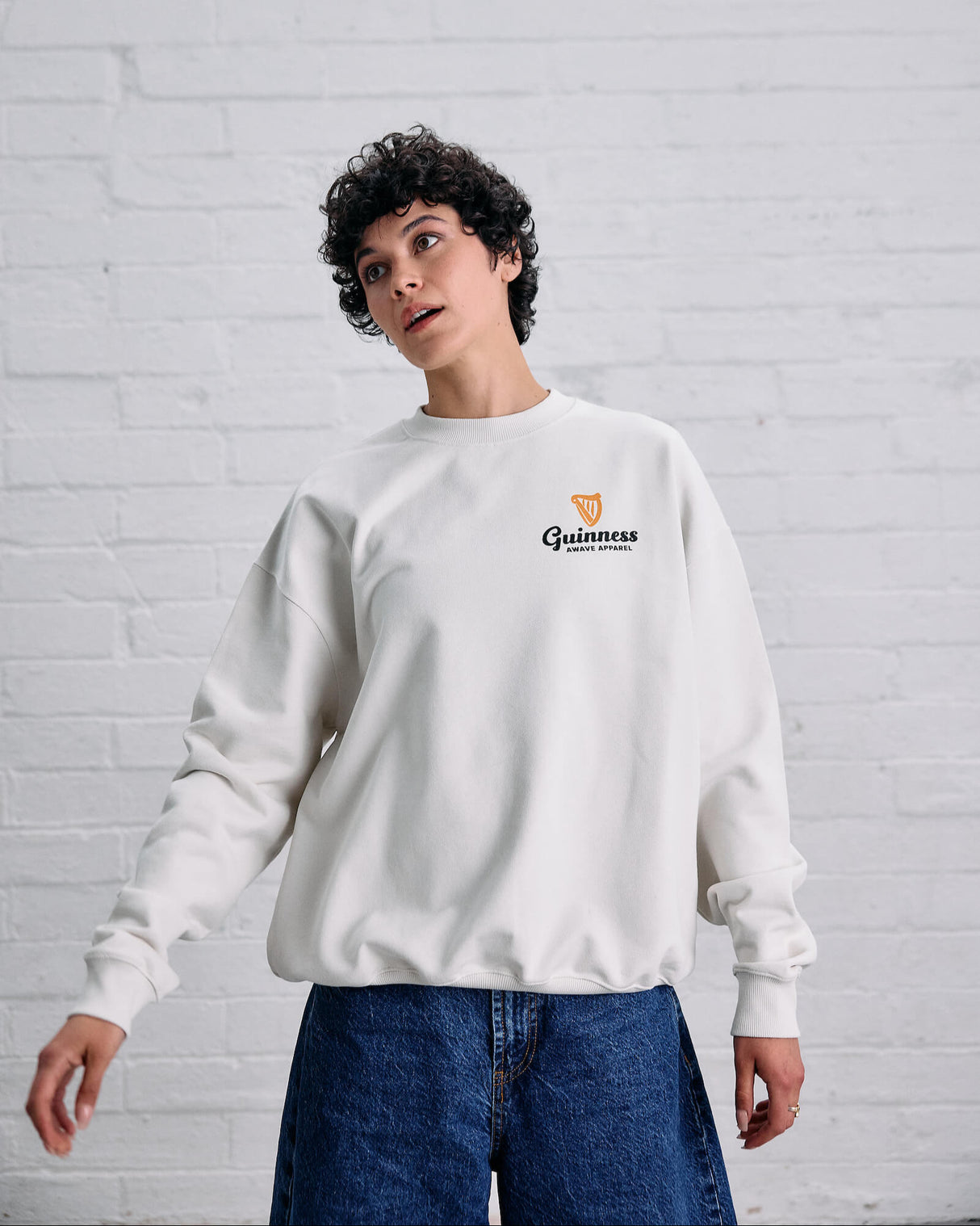 Person wearing a white Guinness sweatshirt against a white brick wall.