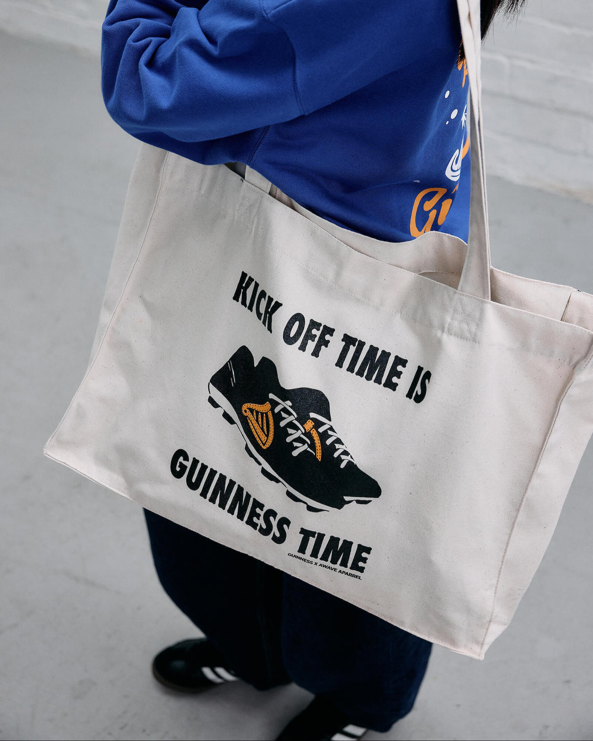 Model wearing the Guinness x Awave Apparel exclusive reusable bag featuring the Kick Off Time is Guinness Time.