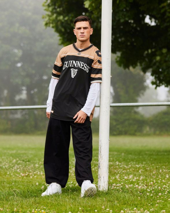 Person wearing a sports jersey standing on a grassy field with trees in the background