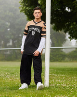 Person wearing a sports jersey standing on a grassy field with trees in the background