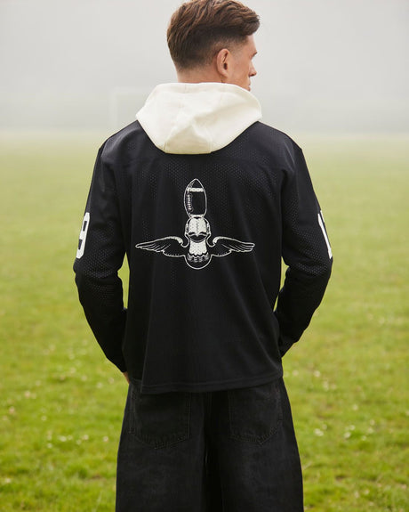 Person wearing a black hoodie with a white graphic on the back, standing in a grassy field.