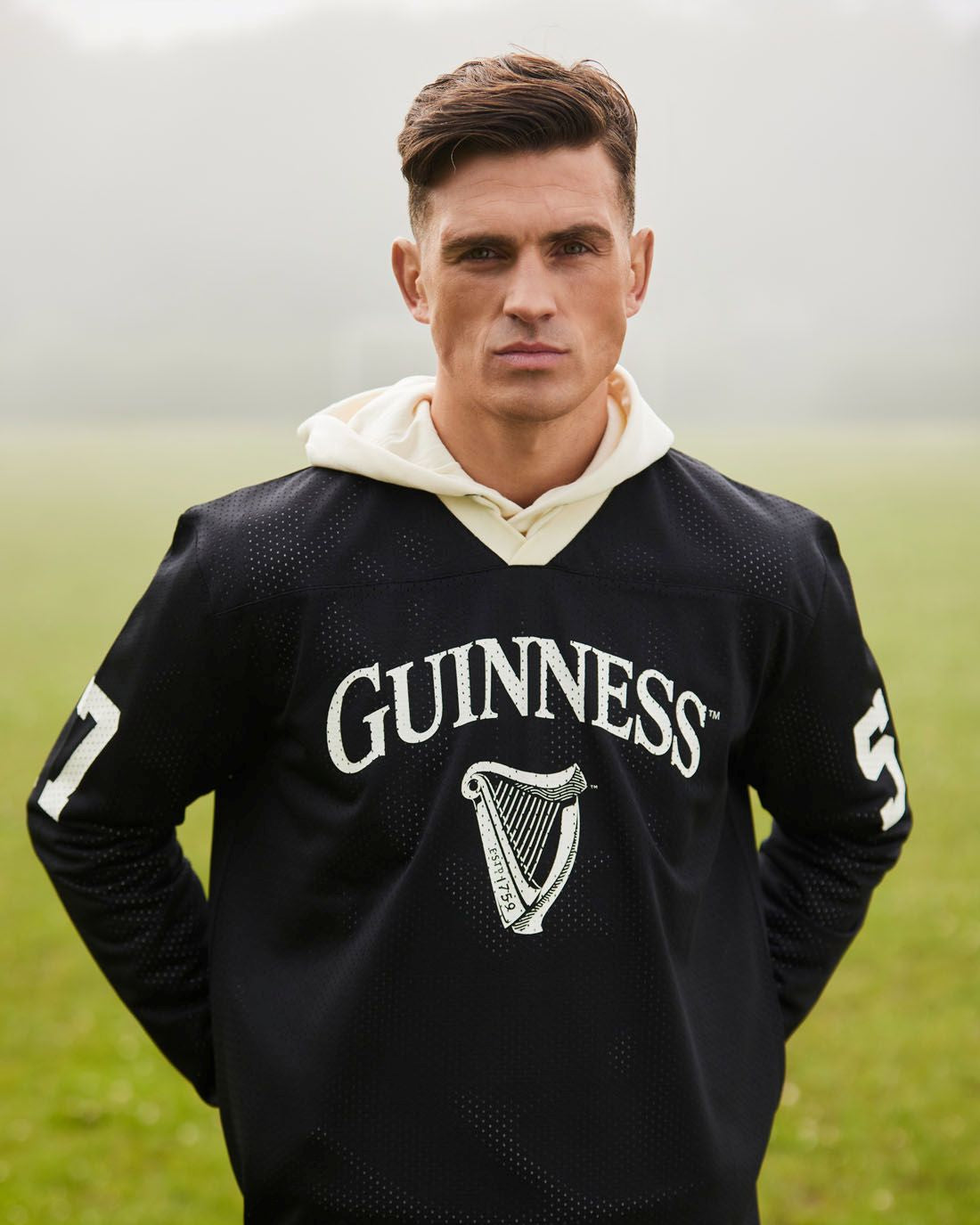 Man wearing a black Guinness hoodie with a white logo in a grassy field