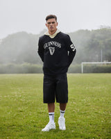 Person wearing a black Guinness hoodie and shorts on a grassy field