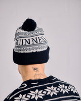Person wearing a black and white patterned beanie with 'Guinness' branding on a gray background.