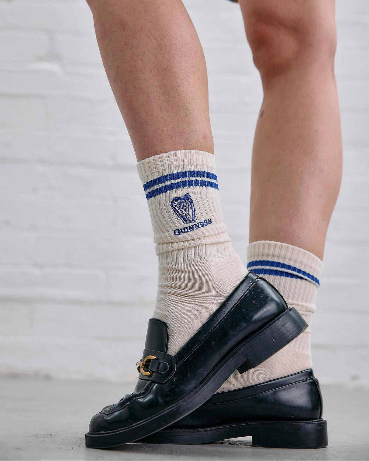 White socks with blue stripes and a logo worn with black loafers on a light gray background