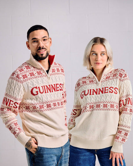 Two people wearing cream Guinness sweaters with red text and patterns against a plain background.