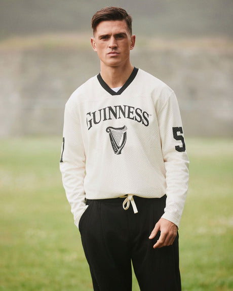 Man wearing a white Guinness sweater with black pants on a grassy field.