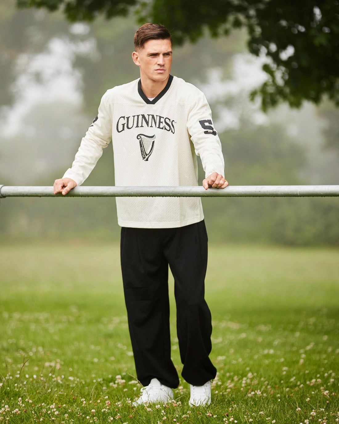 Man wearing a Guinness sweatshirt standing outdoors with trees and grass in the background