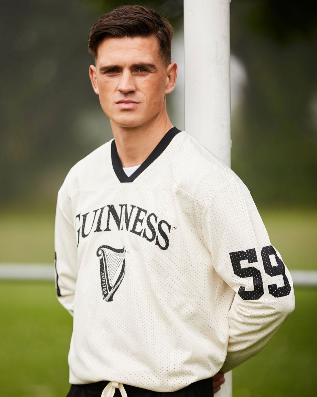 Man wearing a white sports jersey with 'Guinness' and number '59' on a grassy field.