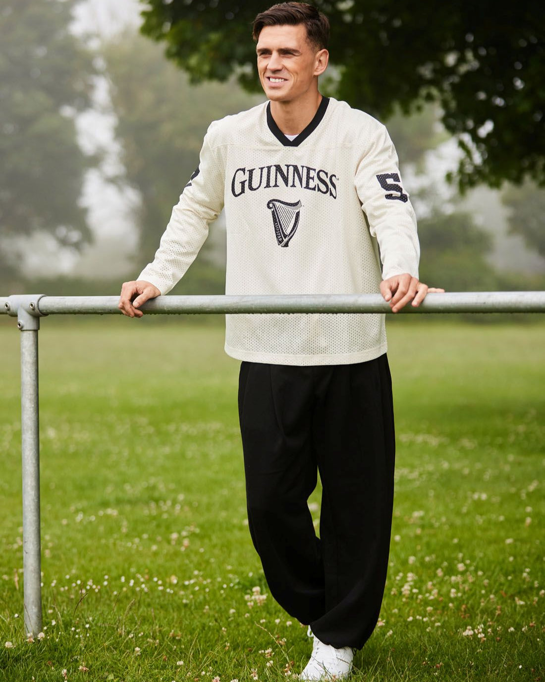 Man wearing a Guinness sweater standing outdoors on a grassy field.