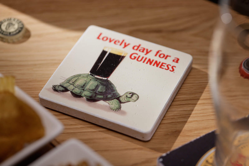 Coaster with turtle illustration and 'Lovely day for a GUINNESS' text on a wooden table.