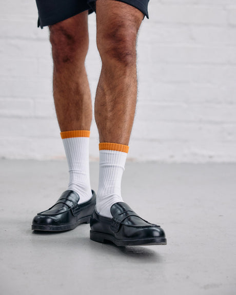 Person wearing black loafers, white socks with orange accents, and black shorts with 'Guinness' logo.