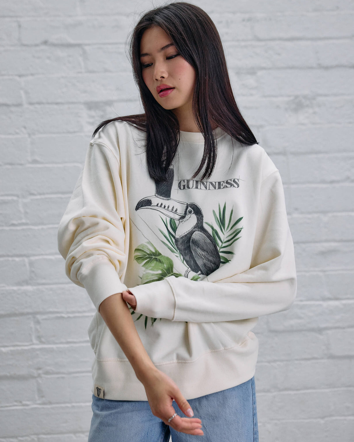 Woman wearing a white sweatshirt with a graphic design against a light gray brick wall.