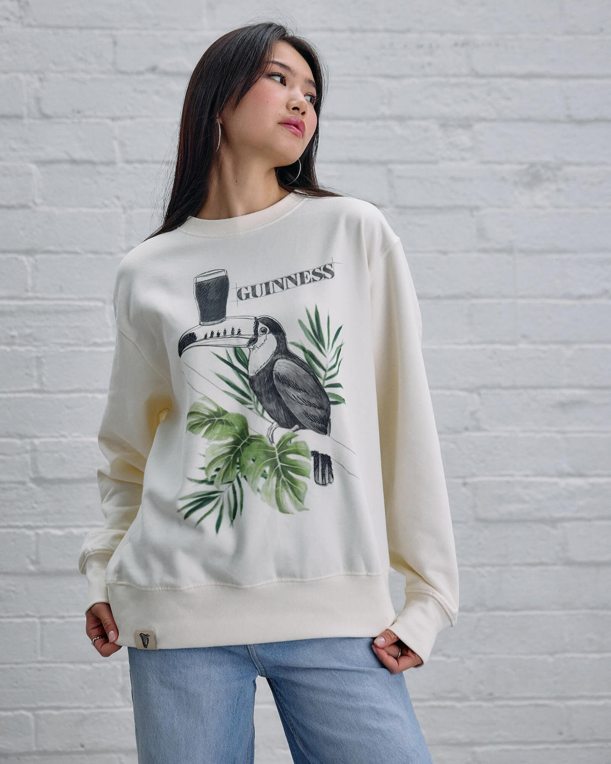 Woman wearing a white sweatshirt with a graphic design against a white brick wall.
