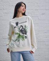 Woman wearing a white sweatshirt with a graphic design against a white brick wall.