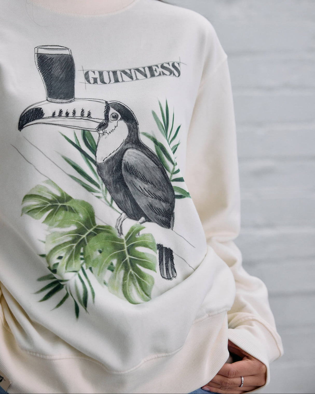 White sweatshirt with a graphic design of a toucan and 'Guinness' branding on a gray background.