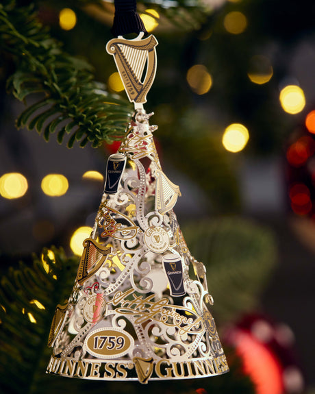 Decorative bell ornament with intricate designs and a harp symbol, hanging on a Christmas tree.