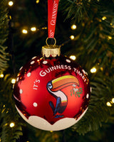 Red ornament with 'It's Guinness Time' text and toucan design on a Christmas tree.