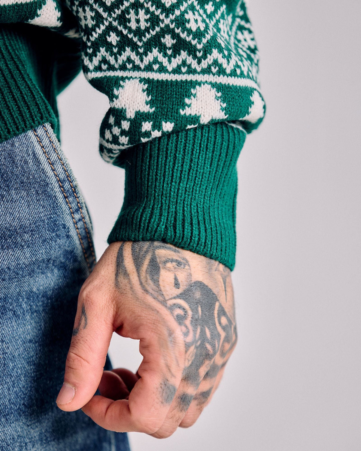 Person wearing a green sweater with a pattern, holding a small object, on a plain background