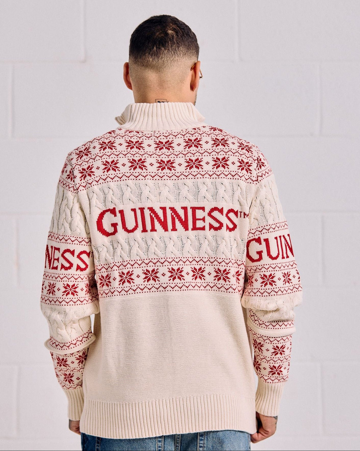 Person wearing a cream sweater with red 'Guinness' text and patterns against a white background