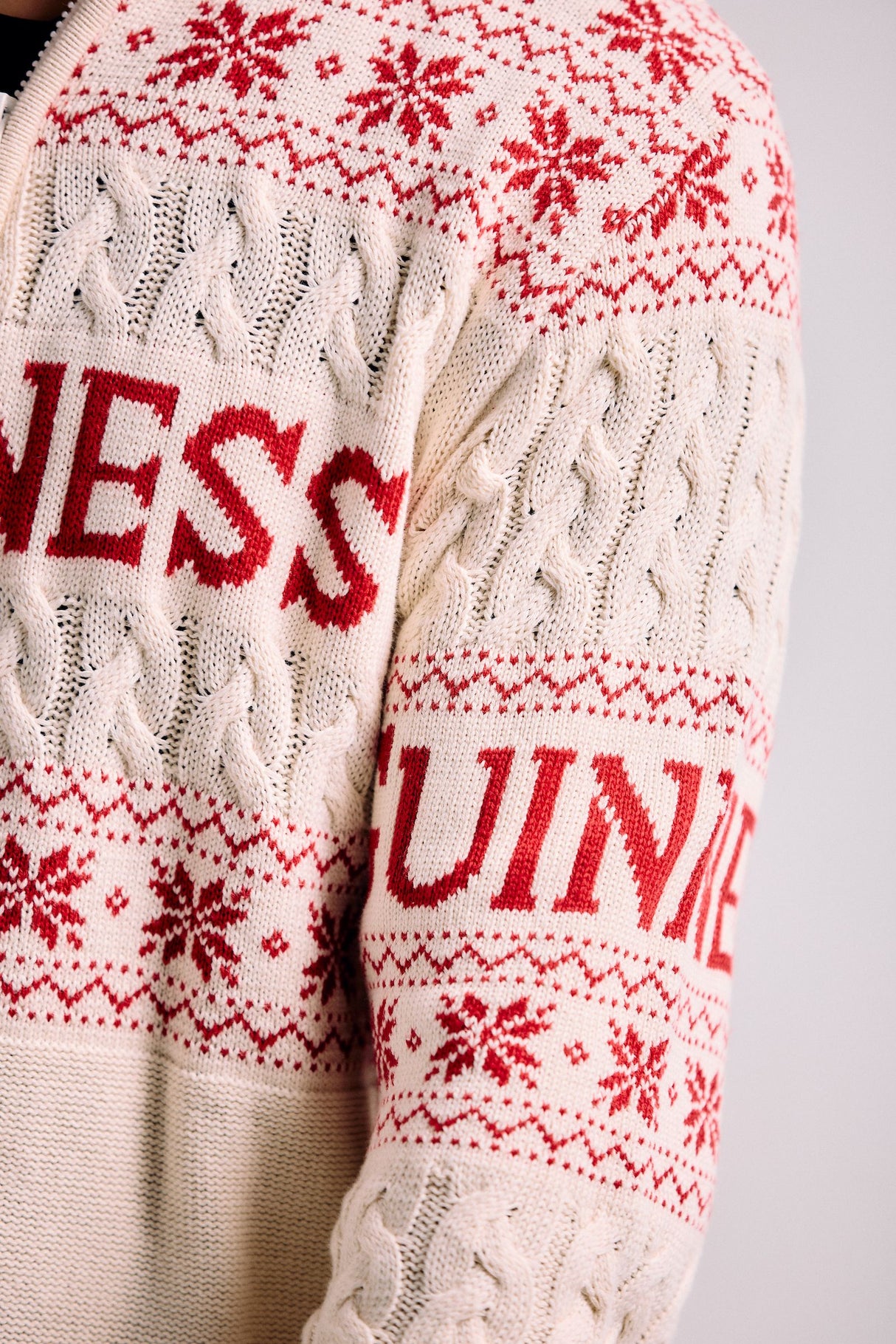 White sweater with red snowflake pattern and 'WESS GUINNE' text on a plain background