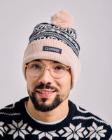 Man wearing a knit beanie with a pom-pom and a sweater with a visible brand logo on a plain background