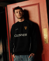 Person wearing a black Guinness sweatshirt standing in front of a red door.
