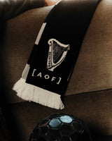 Black scarf with a white emblem and text draped over a brown surface