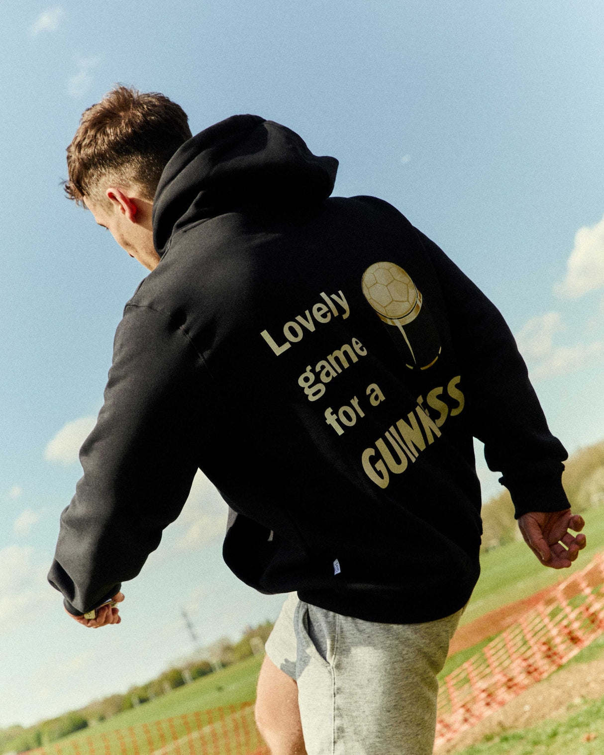 Person wearing a black hoodie with text on the back, standing outdoors with a clear sky.