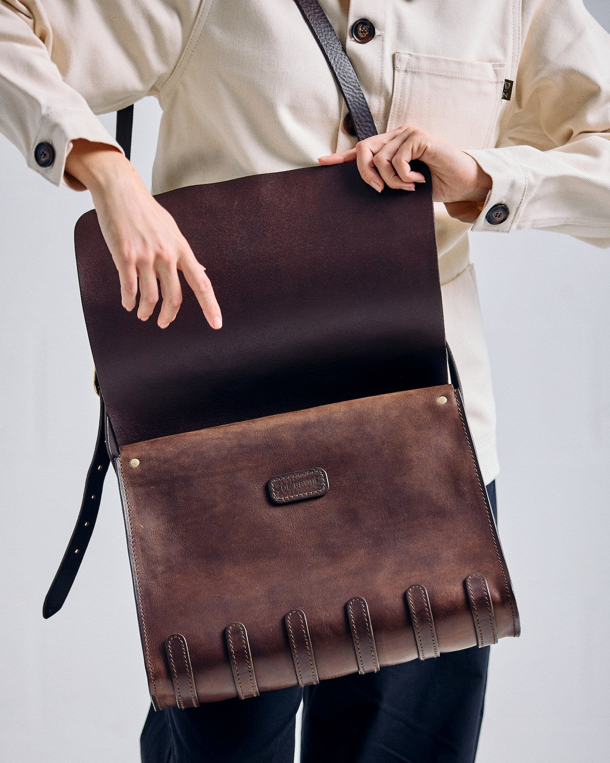 Person holding a brown leather bag against a plain background