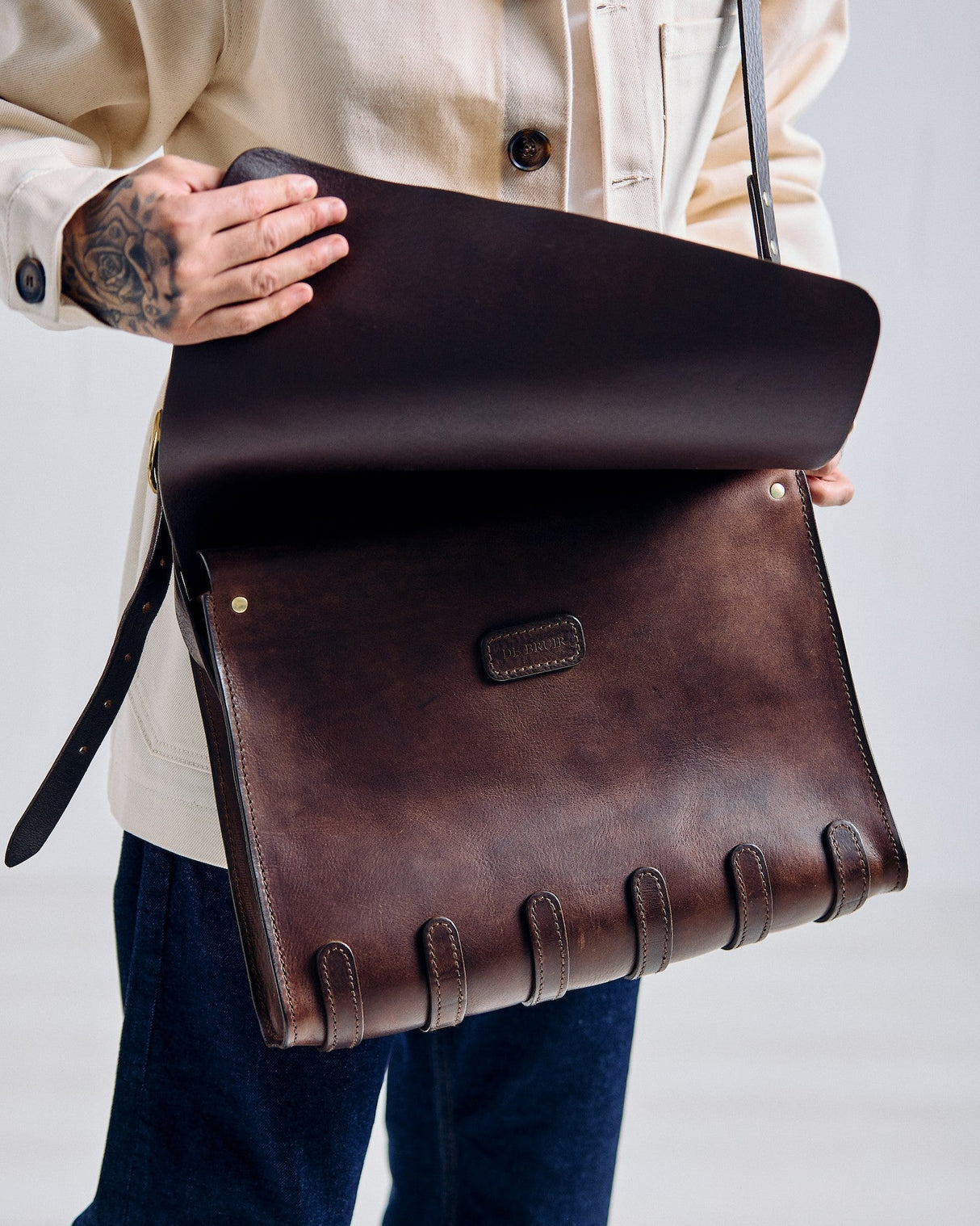 Brown leather bag held by a person against a plain background