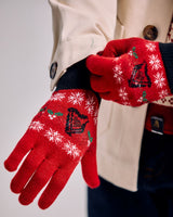 Red gloves with snowflake and bell pattern worn by a person in a beige coat.