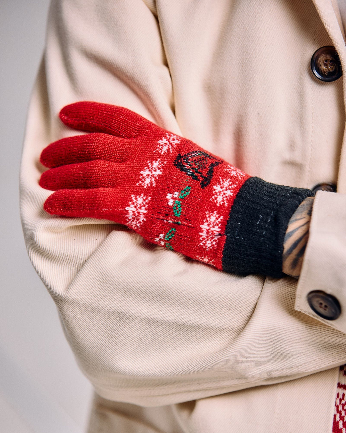 Red embroidered glove on a person wearing a beige coat with a white background