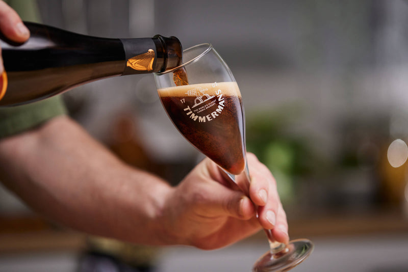 Pouring of the Guinness and Timmermans beer in the Timmermans glass.