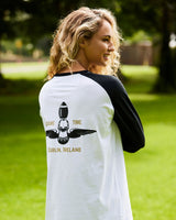 Woman wearing a white and black baseball shirt with a graphic and text on the back, standing outdoors.