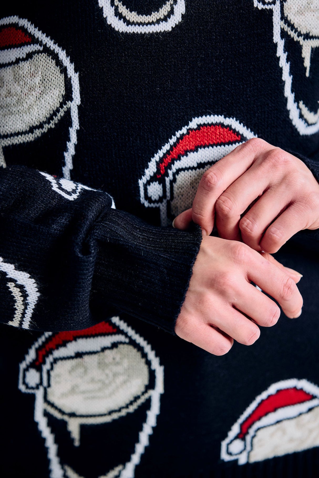 Close-up of a dark sweater with white sheep wearing red hats pattern.