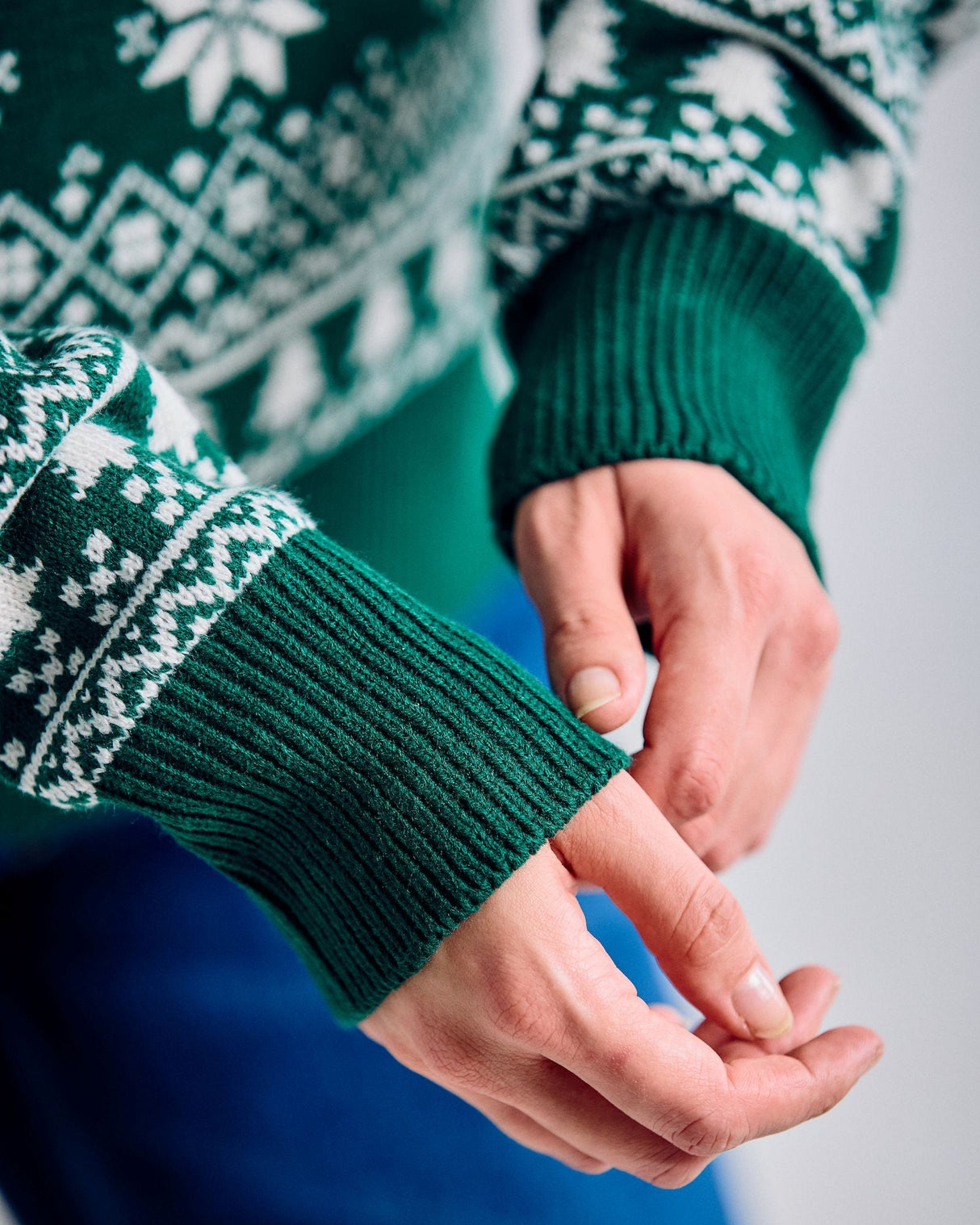 Close-up of a person wearing a green sweater with white patterns, focusing on the sleeve and hands.
