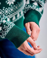 Close-up of a person wearing a green sweater with white patterns, focusing on the sleeve and hands.