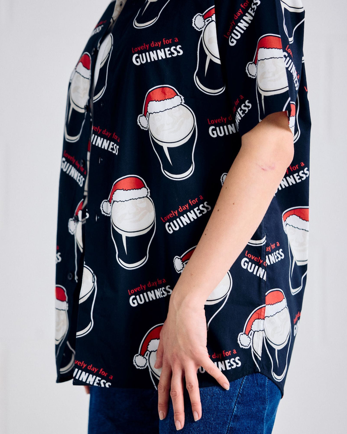 Person wearing a black shirt with Guinness beer bottle and Santa hat pattern on a plain background