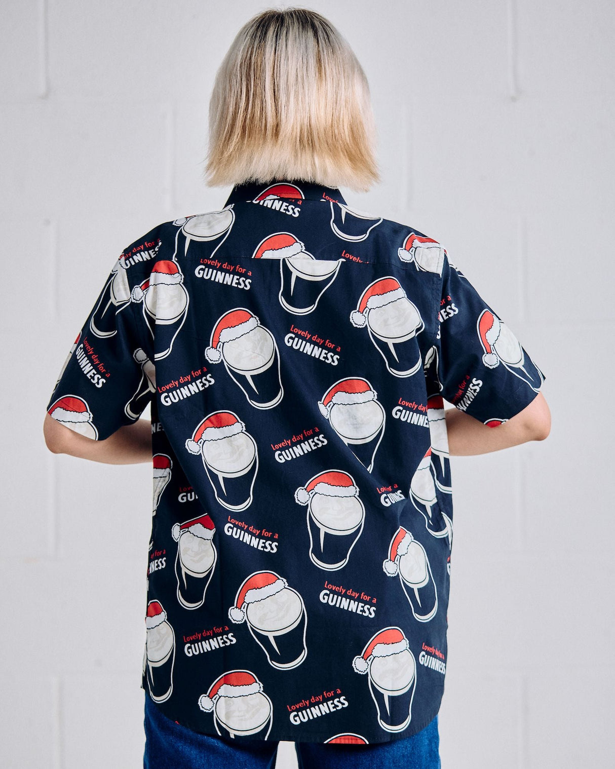 Person wearing a navy blue shirt with Guinness logo and Santa hats on a plain background