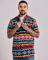 Man wearing a colorful patterned shirt with visible branding against a white brick wall.