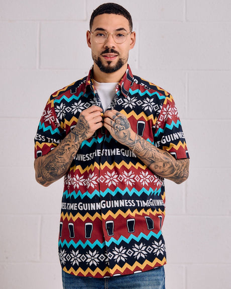Man wearing a colorful patterned shirt with visible branding against a white brick wall.