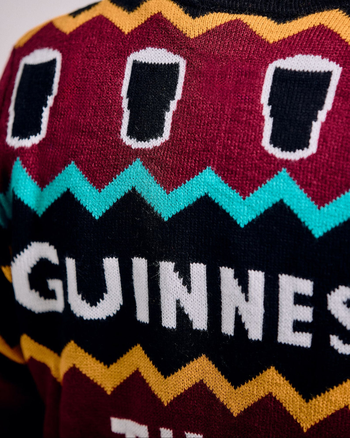 Close-up of a sweater with Guinness beer design featuring black beer pints on a colorful pattern.