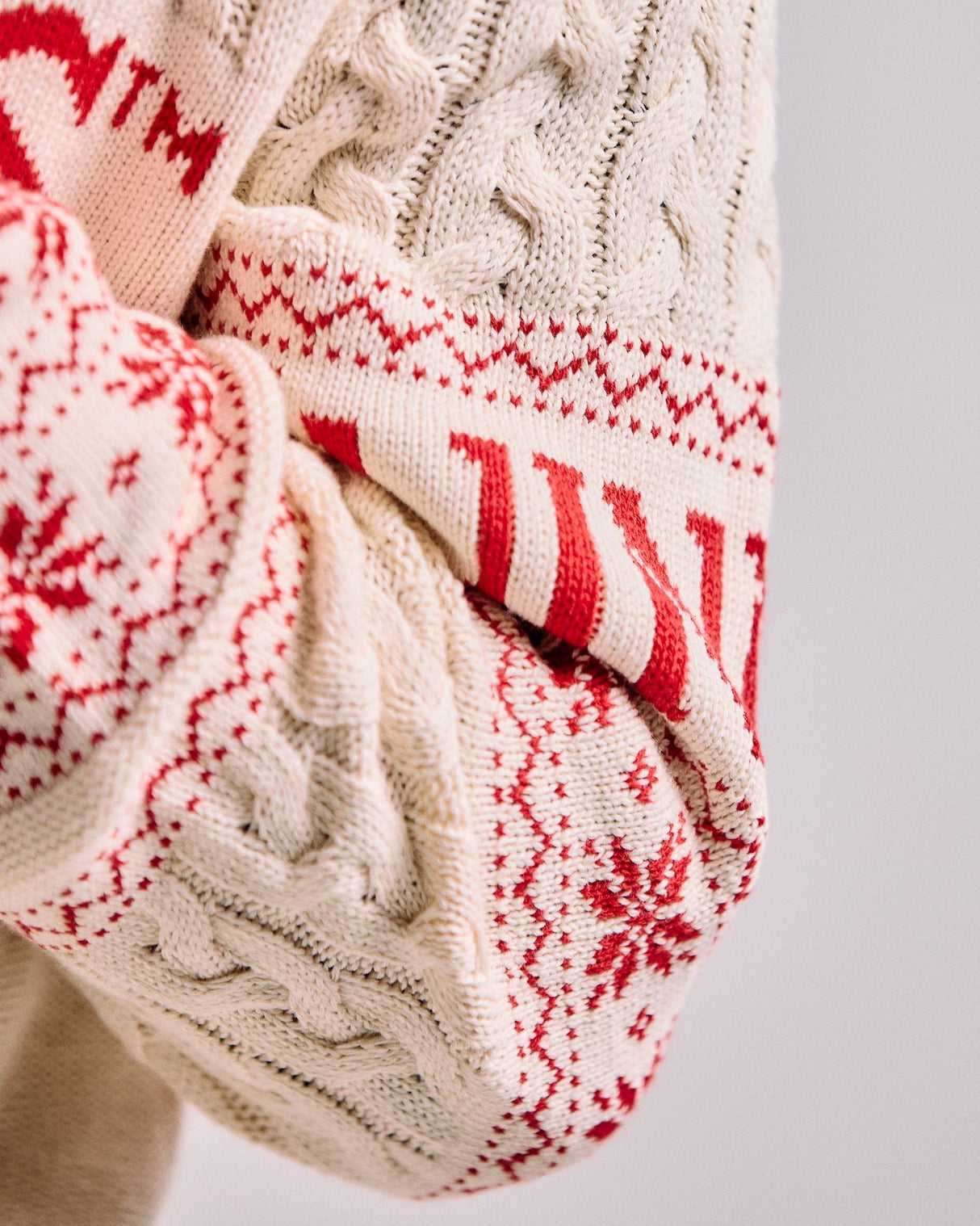 Close-up of a cream-colored knitted sweater with red pattern on a light gray background