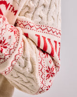 Close-up of a cream-colored knitted sweater with red pattern on a light gray background
